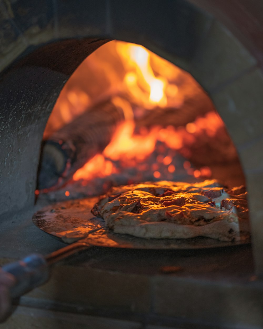 Le four à bois allumé, une pizza sur la pelle