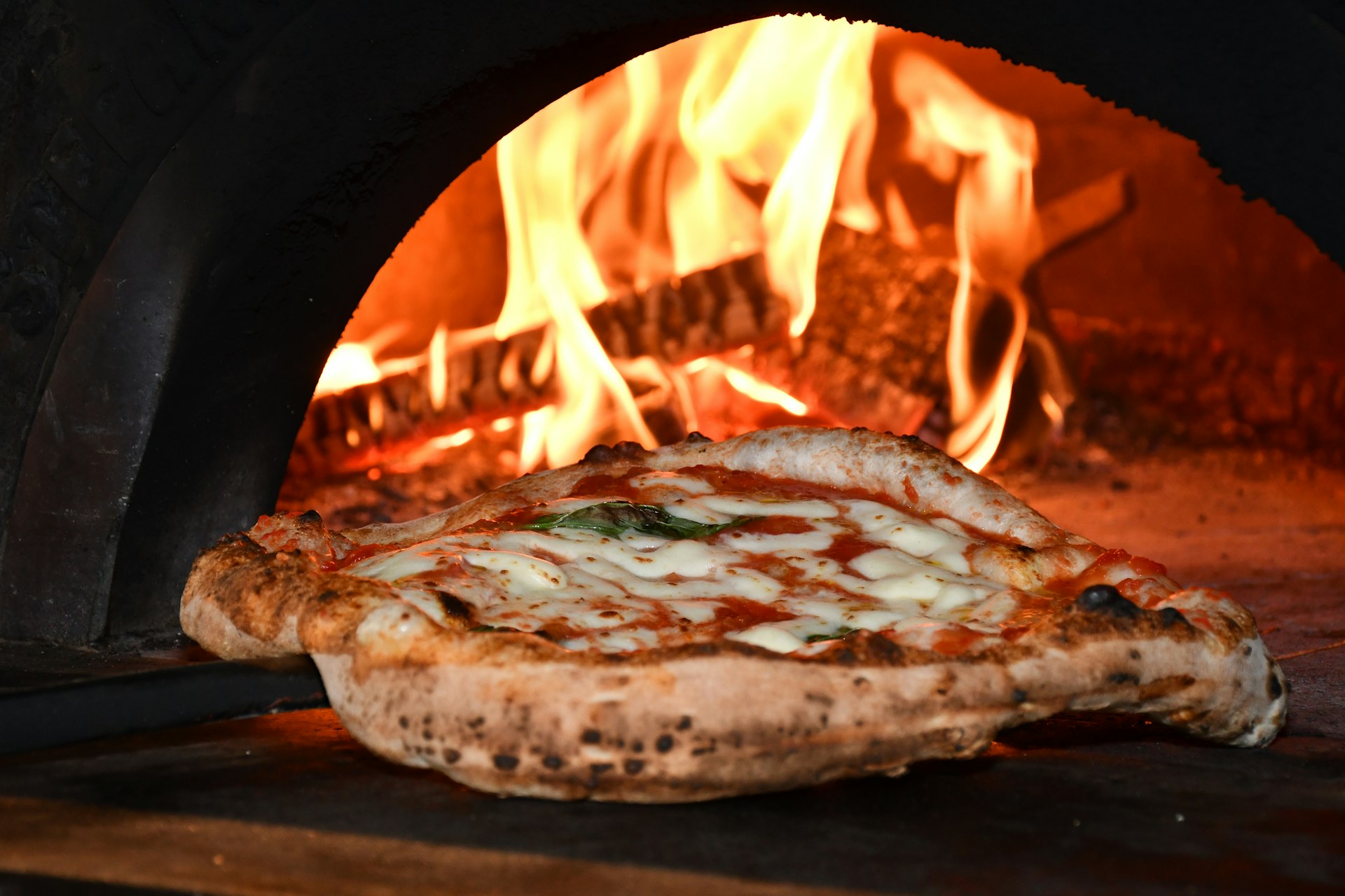 Une pizza napolitaine qui cuit dans les flammes du four à bois